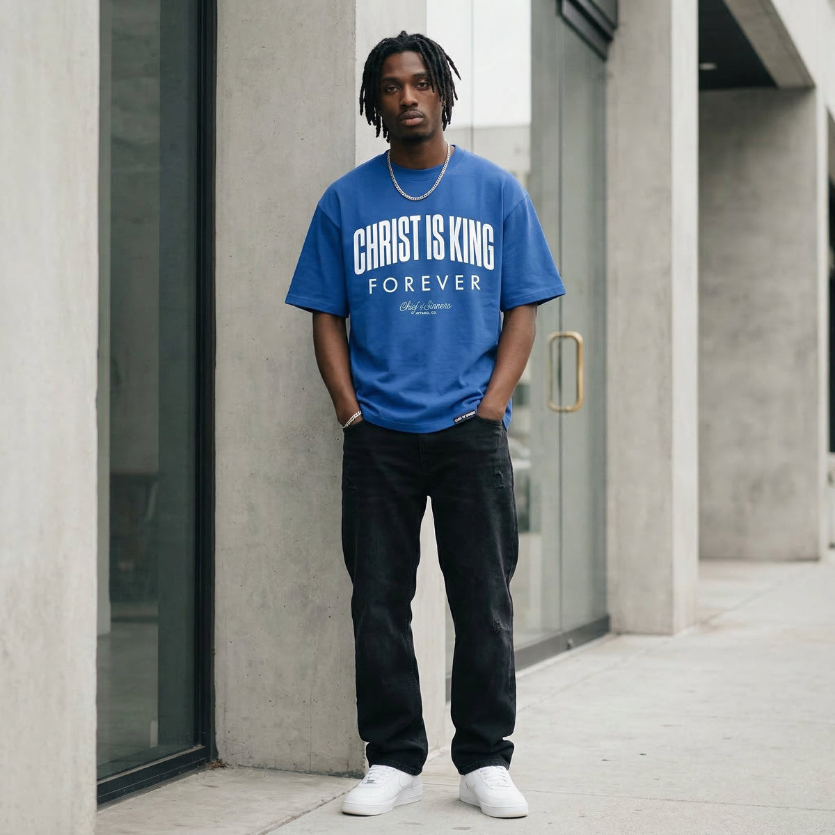 Premium streetwear campaign image of a model wearing the royal blue Christ Is King heavyweight tee in a clean concrete setting.